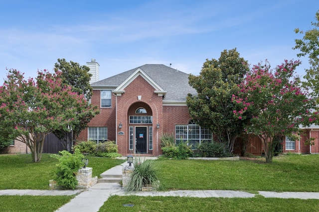 view of front of house with brick siding, a chimney, and a front yard