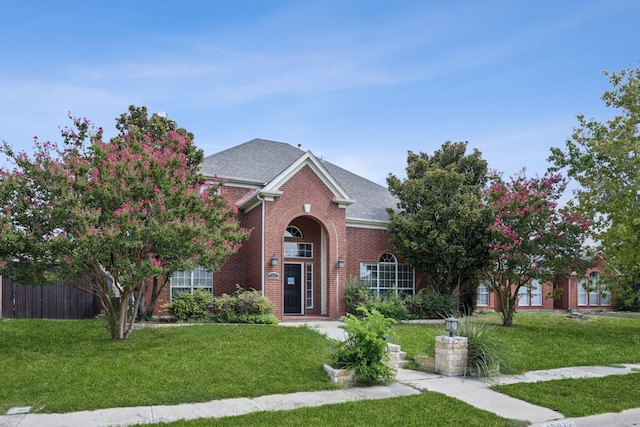 traditional home with roof with shingles, fence, a front lawn, and brick siding