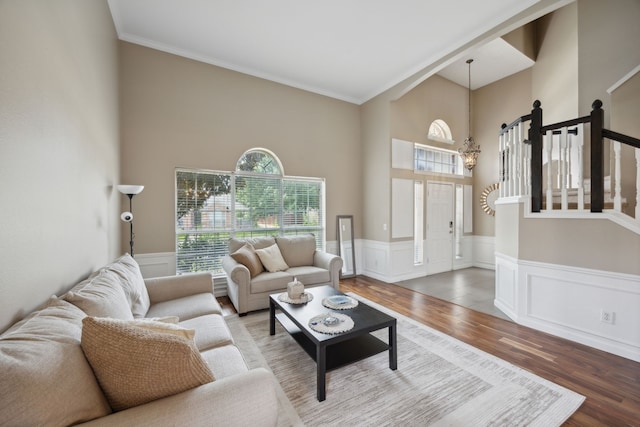living area with ornamental molding, wainscoting, a towering ceiling, and wood finished floors