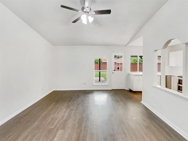 spare room with baseboards, a ceiling fan, arched walkways, and wood finished floors