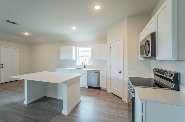 kitchen with a sink, stainless steel appliances, light wood-type flooring, a kitchen island, and visible vents