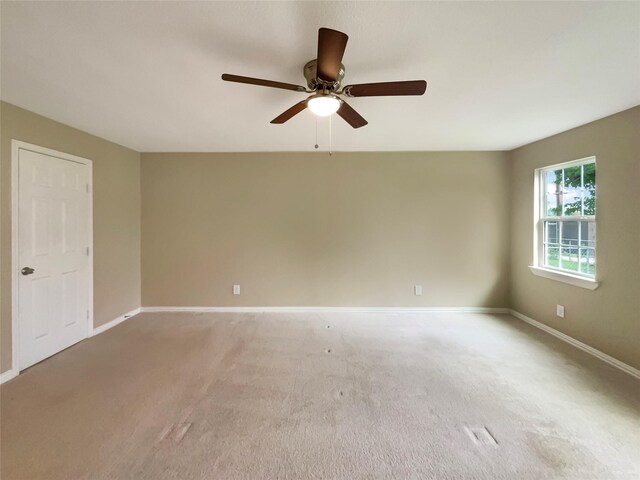 spare room with light colored carpet, a ceiling fan, and baseboards