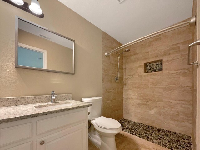 bathroom with visible vents, a tile shower, toilet, and vanity
