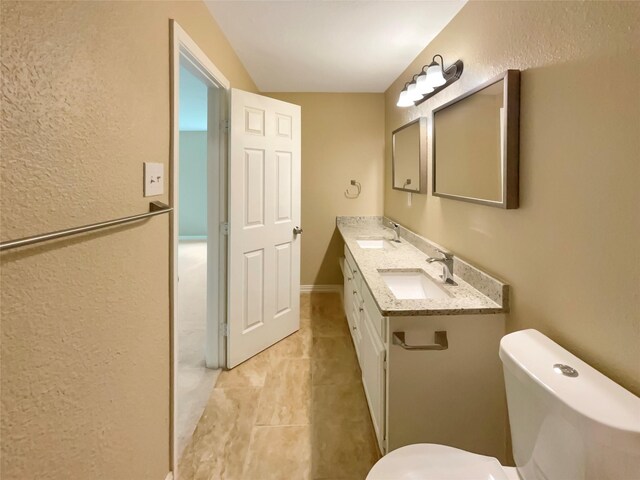 bathroom featuring toilet, a textured wall, a sink, and tile patterned flooring