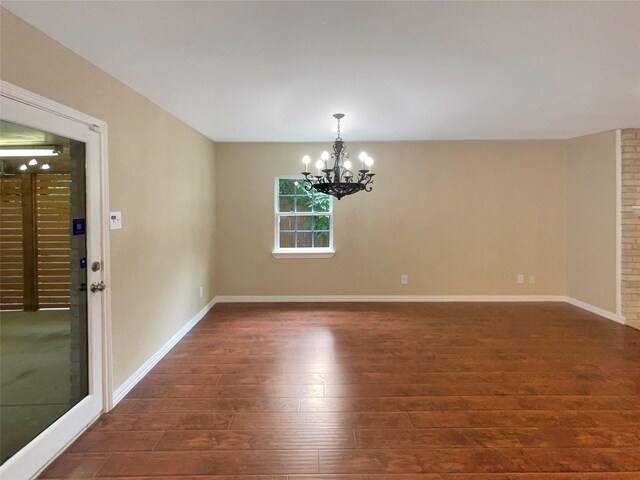 unfurnished room featuring a chandelier, baseboards, and dark wood finished floors