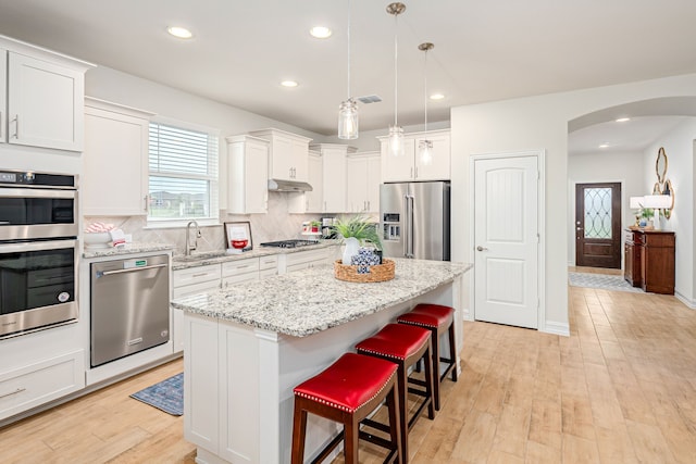 kitchen featuring a sink, a kitchen island, a kitchen breakfast bar, arched walkways, and appliances with stainless steel finishes