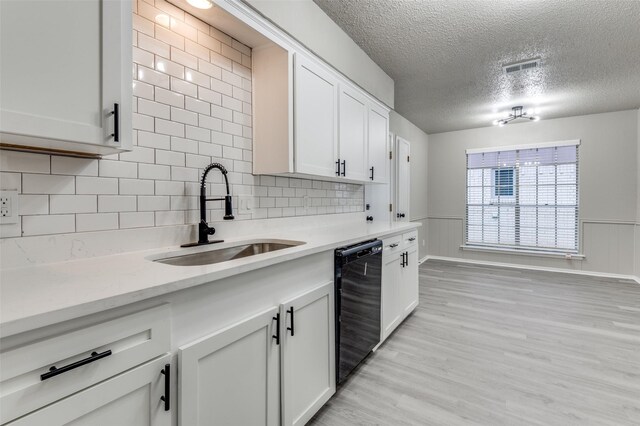 kitchen with a sink, dishwasher, a textured ceiling, light wood-style flooring, and white cabinetry