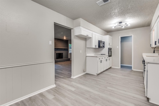 kitchen featuring white cabinets, a sink, light wood-style floors, visible vents, and black appliances