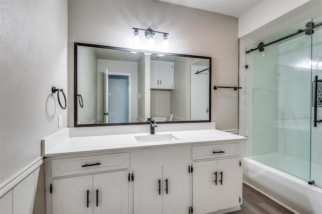 bathroom featuring vanity, a textured wall, bath / shower combo with glass door, and wood finished floors