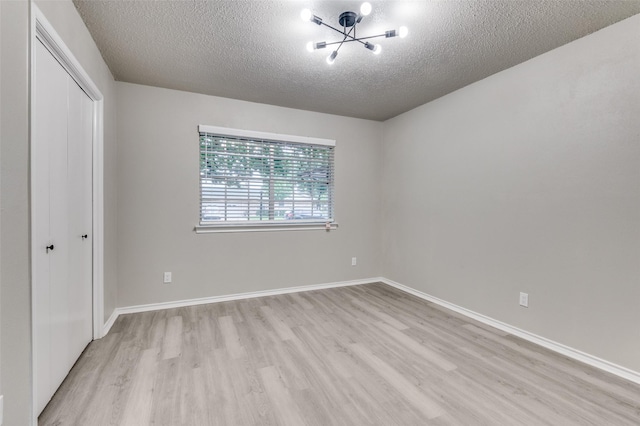 unfurnished bedroom with light wood finished floors, a textured ceiling, a chandelier, baseboards, and a closet