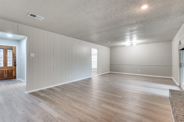 unfurnished room with baseboards, a textured ceiling, visible vents, and light wood-style flooring
