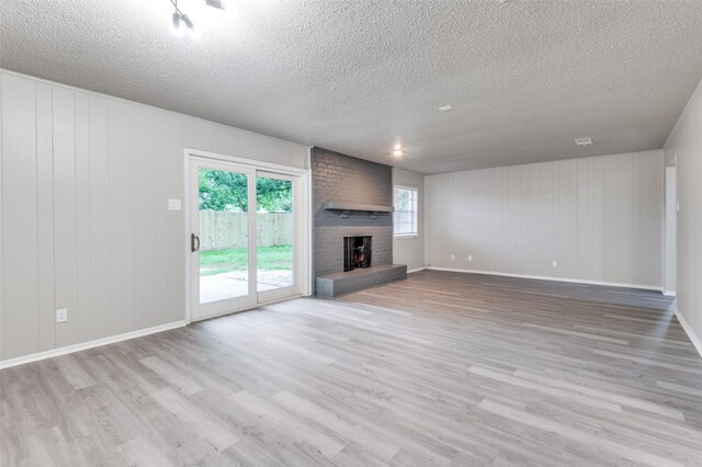 unfurnished living room featuring a brick fireplace, a textured ceiling, baseboards, and wood finished floors