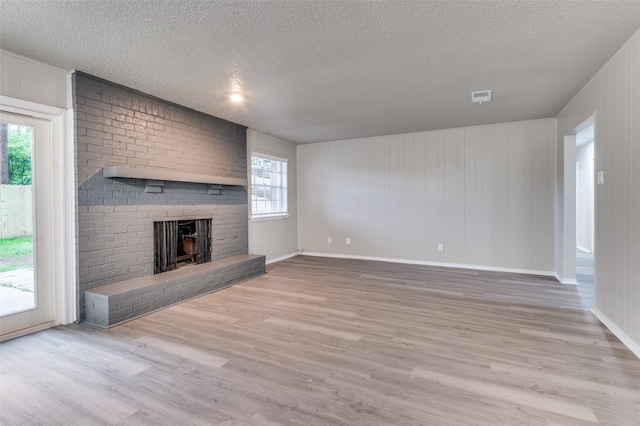 unfurnished living room featuring a brick fireplace, visible vents, plenty of natural light, and wood finished floors