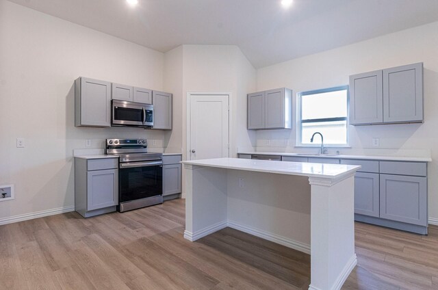 kitchen with a sink, appliances with stainless steel finishes, gray cabinets, and light wood-type flooring
