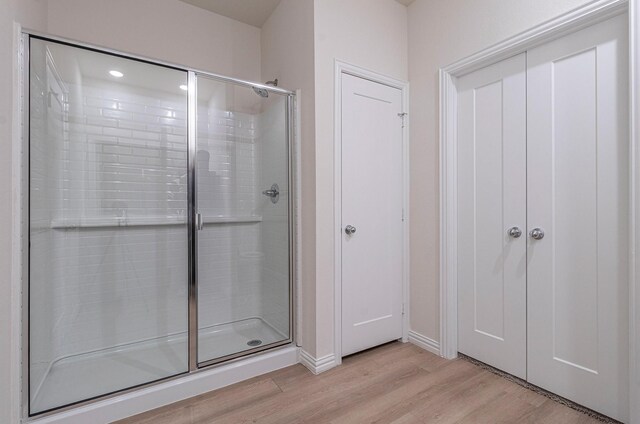 bathroom with recessed lighting, baseboards, a shower stall, and wood finished floors