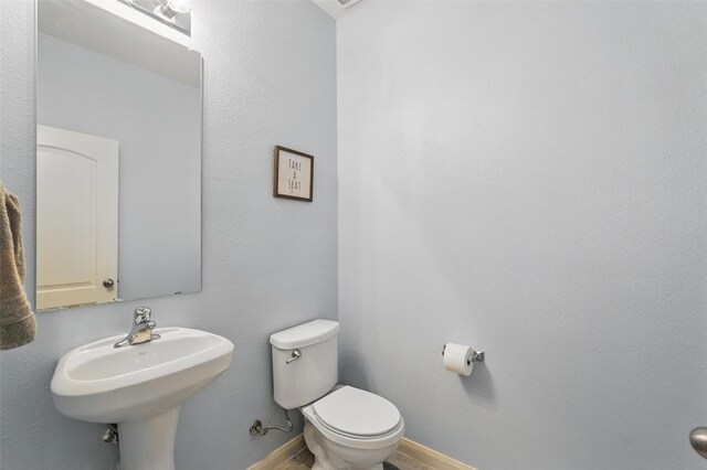half bathroom with toilet, a sink, and baseboards