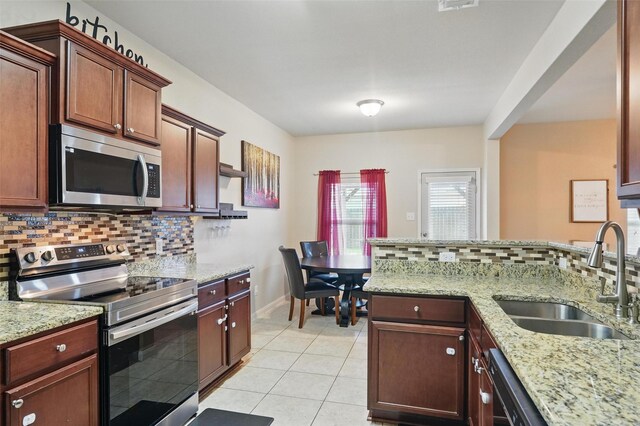 kitchen featuring appliances with stainless steel finishes, a sink, backsplash, light tile patterned floors, and light stone countertops