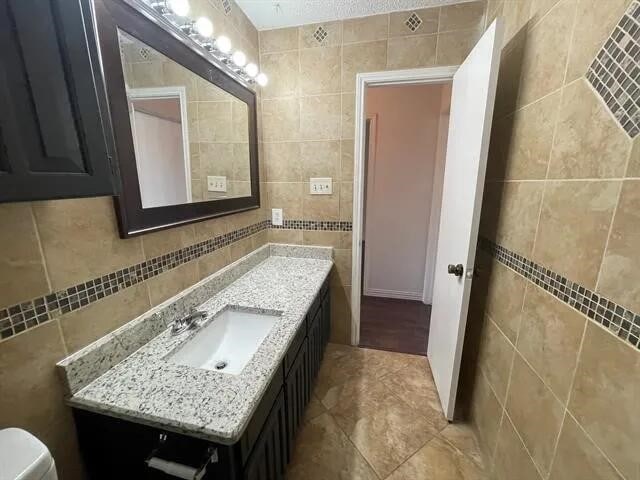 2406 Parkside Dr, Grand Prairie, TX 75052 - bathroom with toilet, tile walls, tile patterned flooring, and vanity