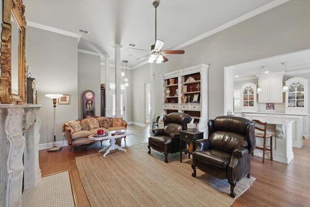living room featuring a ceiling fan, visible vents, wood finished floors, a high ceiling, and ornamental molding
