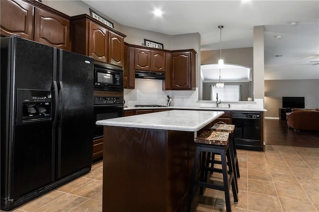 kitchen featuring light countertops, backsplash, a kitchen bar, under cabinet range hood, and black appliances