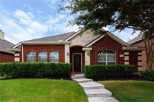 single story home featuring roof with shingles, stone siding, brick siding, and a front yard