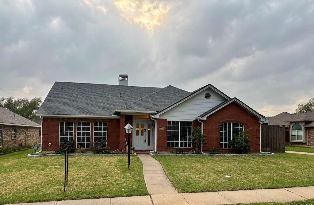 view of front of house featuring brick siding, a shingled roof, a chimney, and a front yard