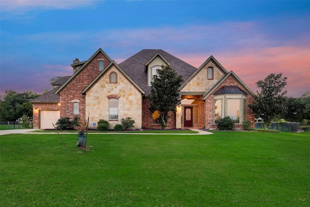 french country inspired facade featuring an attached garage, concrete driveway, a front lawn, and stone siding