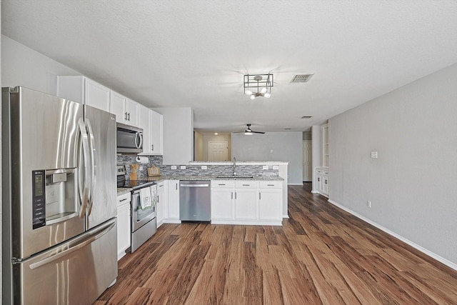 1225 Bellevue Dr, Princeton, TX 75407 - kitchen featuring dark wood-style flooring, a peninsula, white cabinets, a sink, and stainless steel appliances