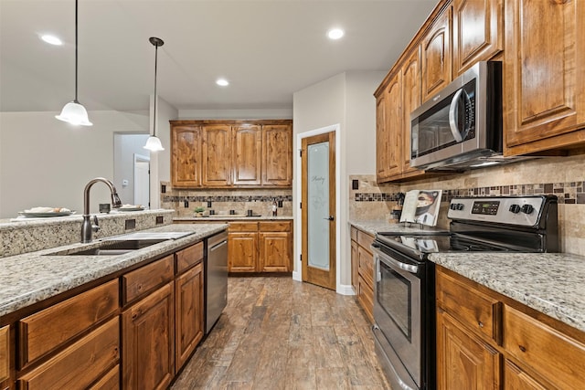kitchen with pendant lighting, tasteful backsplash, light stone countertops, a sink, and stainless steel appliances