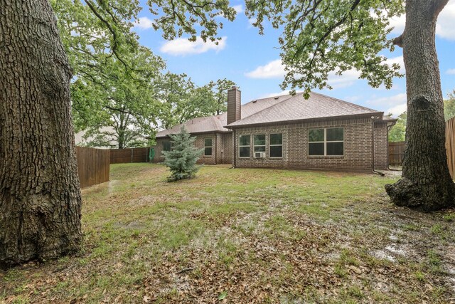 back of house featuring roof with shingles, brick siding, a fenced backyard, a chimney, and a yard