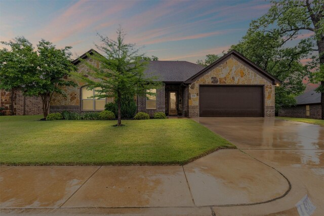 view of front of property with an attached garage, a front yard, driveway, and stone siding