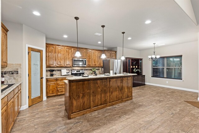 kitchen with a notable chandelier, appliances with stainless steel finishes, baseboards, backsplash, and a center island with sink