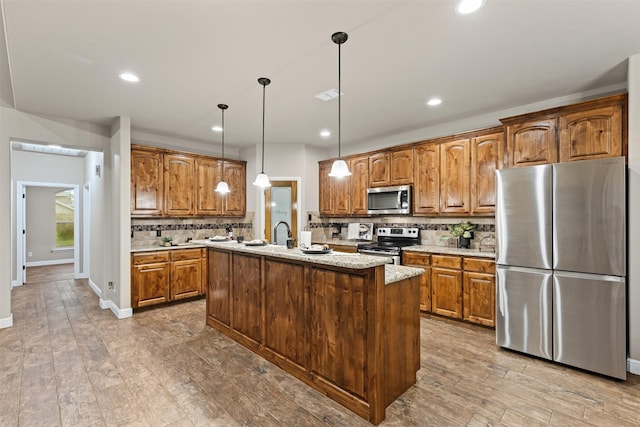 kitchen with tasteful backsplash, a kitchen island with sink, stainless steel appliances, and brown cabinetry
