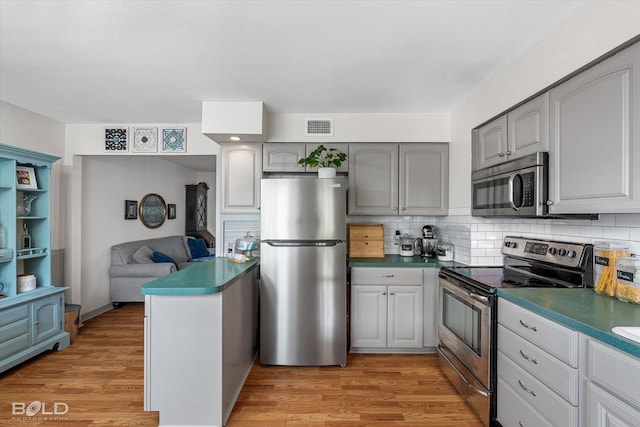 kitchen featuring gray cabinets, backsplash, visible vents, appliances with stainless steel finishes, and light wood-style flooring