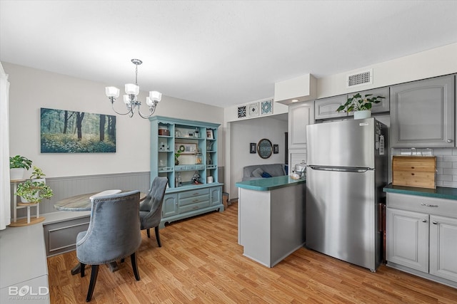 kitchen with light wood-style floors, visible vents, gray cabinetry, freestanding refrigerator, and an inviting chandelier