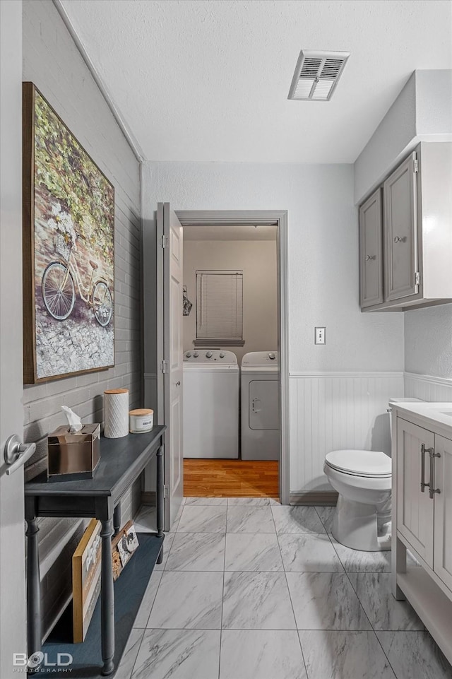 bathroom featuring visible vents, toilet, marble finish floor, and washing machine and clothes dryer