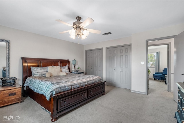 bedroom featuring multiple closets, ceiling fan, light carpet, and visible vents