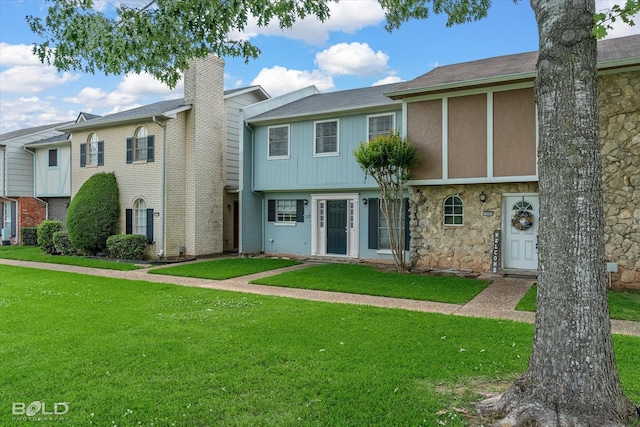 view of property featuring stone siding, a chimney, and a front yard