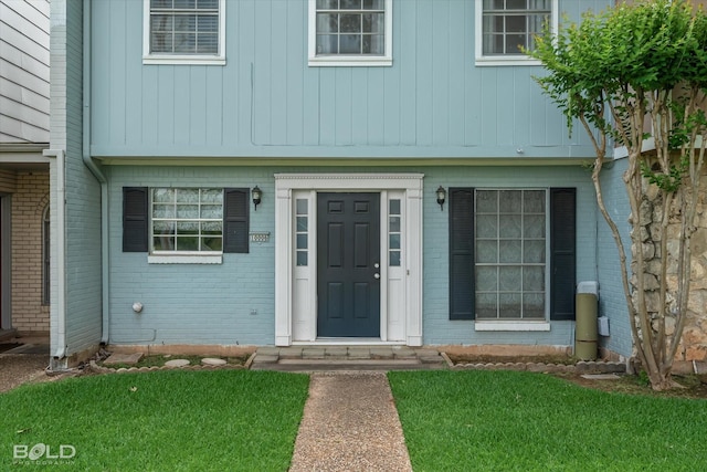 view of exterior entry with a lawn and brick siding