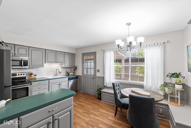 kitchen with a sink, appliances with stainless steel finishes, gray cabinets, and an inviting chandelier