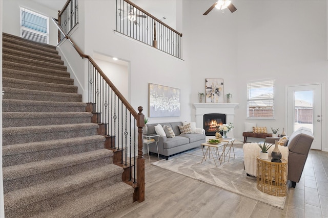 1008 Sublime Dr, Heath, TX 75126 - living room with stairs, a glass covered fireplace, wood finished floors, a high ceiling, and a ceiling fan