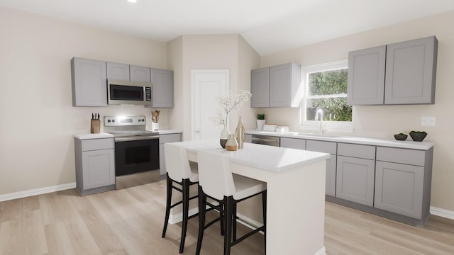 kitchen featuring a kitchen breakfast bar, light countertops, a sink, gray cabinetry, and stainless steel appliances