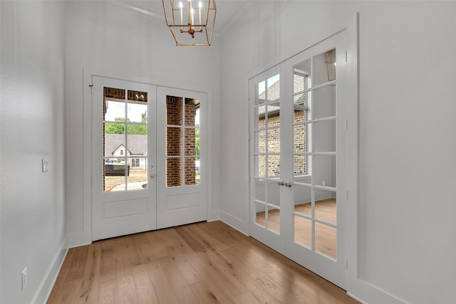 doorway to outside with light wood-style floors, baseboards, an inviting chandelier, and french doors