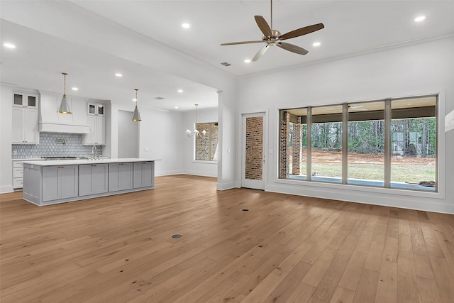 unfurnished living room featuring plenty of natural light, ceiling fan with notable chandelier, and light wood-type flooring