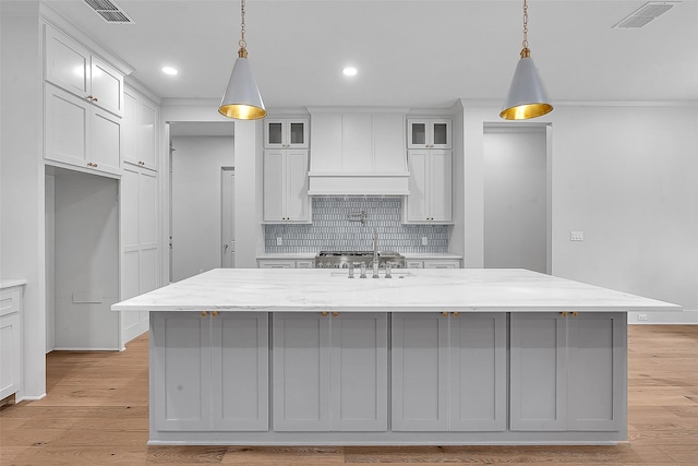 kitchen featuring tasteful backsplash, custom exhaust hood, light wood-style flooring, and visible vents