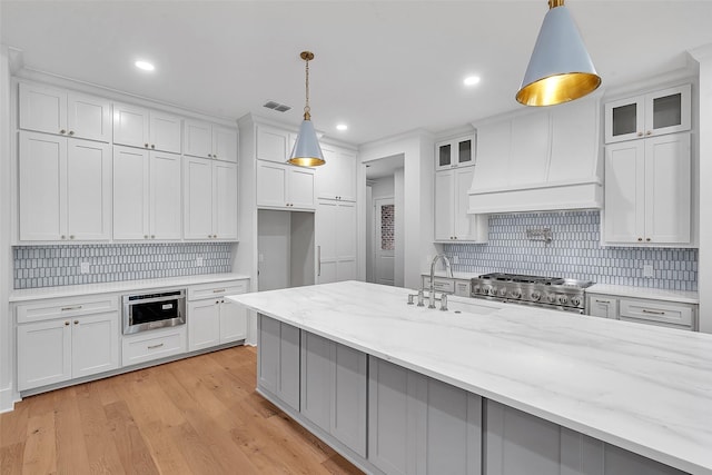 kitchen featuring visible vents, tasteful backsplash, stove, a sink, and premium range hood