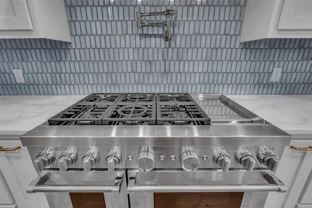 interior details featuring white cabinetry, backsplash, light stone countertops, and range with two ovens