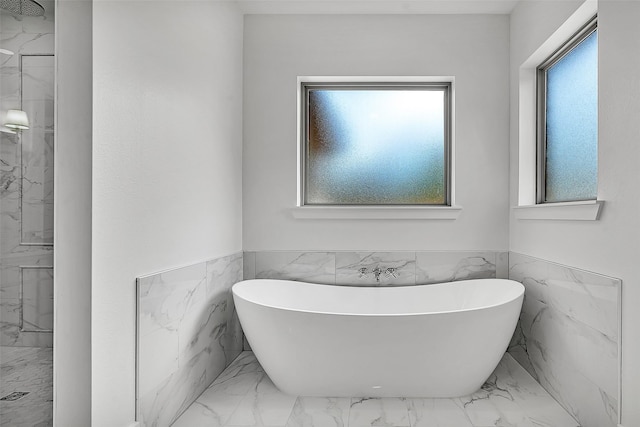 bathroom with marble finish floor, a soaking tub, a marble finish shower, and tile walls