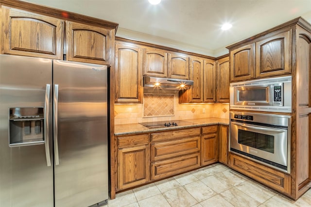 kitchen with appliances with stainless steel finishes, brown cabinetry, decorative backsplash, stone counters, and under cabinet range hood