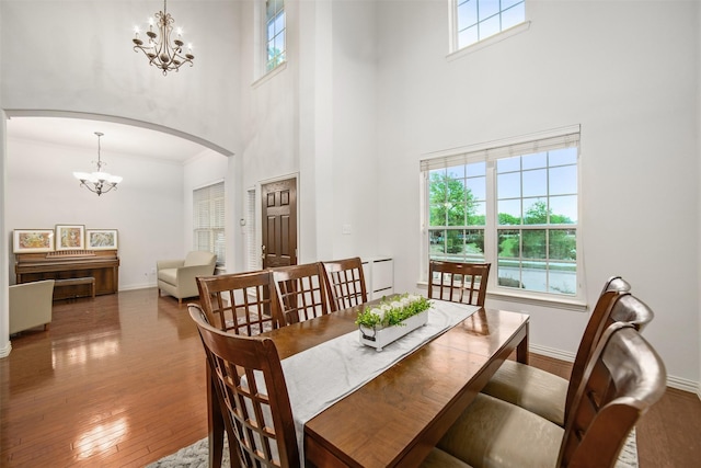 dining room with arched walkways, hardwood / wood-style flooring, a towering ceiling, and a notable chandelier